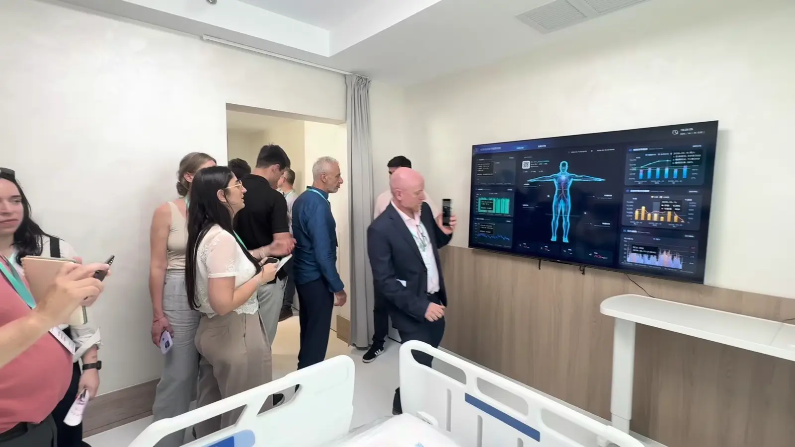 Participantes observam uma cama e uma tela em um ambiente hospitalar em 2026.